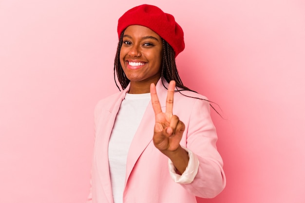 Jovem mulher afro-americana isolada em um fundo rosa alegre e despreocupada, mostrando um símbolo de paz com os dedos.