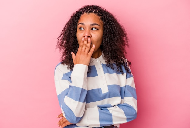 Jovem mulher afro-americana isolada em um fundo rosa bocejando, mostrando um gesto cansado, cobrindo a boca com a mão.