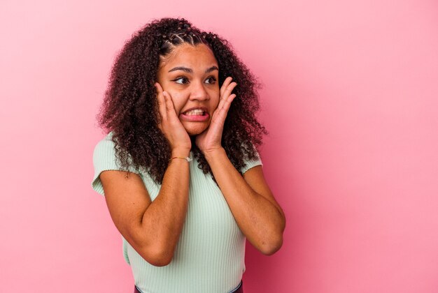 Jovem mulher afro-americana isolada em um fundo rosa com medo e com medo.