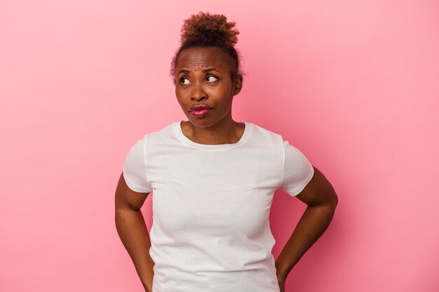 Jovem mulher afro-americana isolada em um fundo rosa confusa, sente-se em dúvida e insegura.