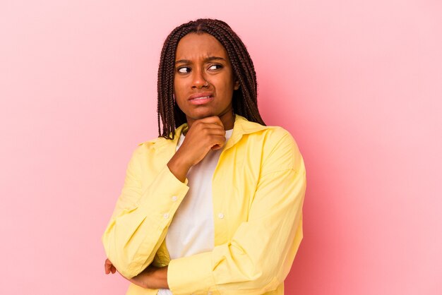 Jovem mulher afro-americana isolada em um fundo rosa confusa, sente-se em dúvida e insegura.