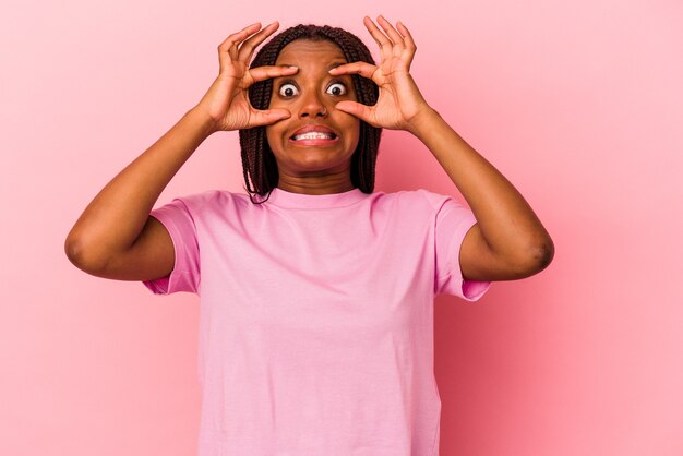 Jovem mulher afro-americana isolada em um fundo rosa, mantendo os olhos abertos para encontrar uma oportunidade de sucesso.