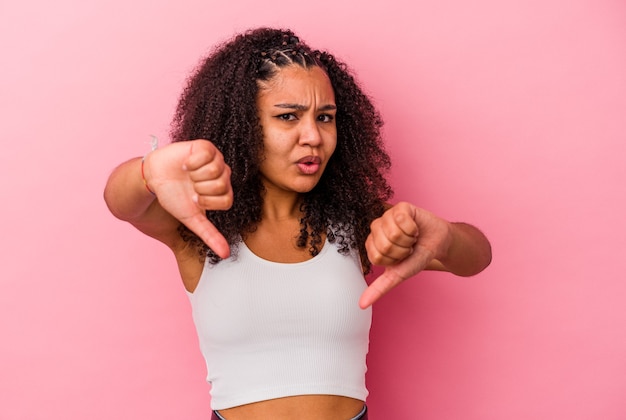 Jovem mulher afro-americana isolada em um fundo rosa, mostrando o polegar para baixo e expressando antipatia.