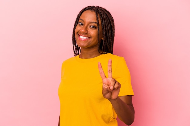 Jovem mulher afro-americana isolada em um fundo rosa, mostrando sinal de vitória e sorrindo amplamente.
