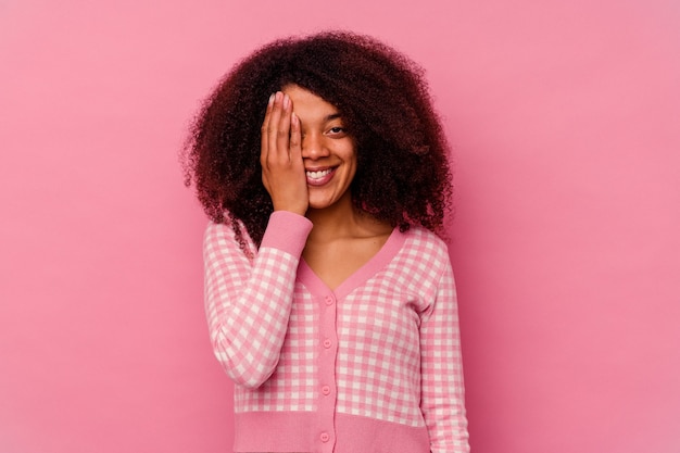 Jovem mulher afro-americana isolada em um fundo rosa, se divertindo, cobrindo metade do rosto com a palma da mão.