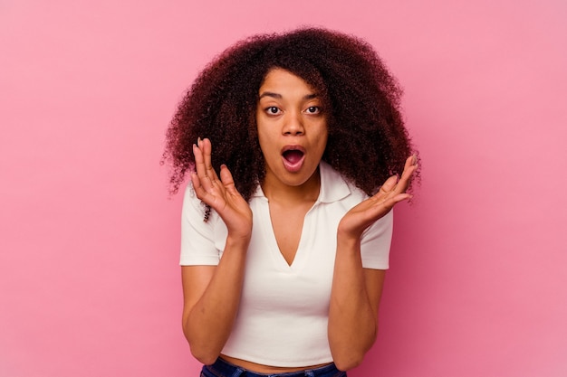 Jovem mulher afro-americana isolada em um fundo rosa surpresa e chocada.