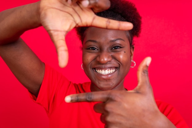 Jovem mulher afro-americana isolada em um fundo vermelho com gesto quadrado da sessão de estúdio de dedos
