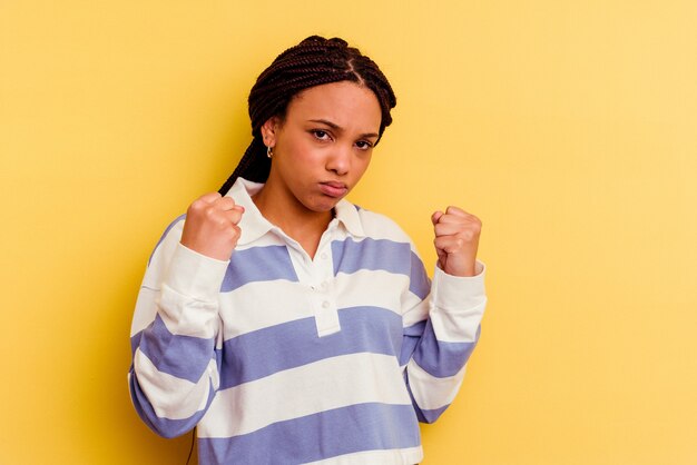 Jovem mulher afro-americana isolada na parede amarela, mostrando o punho, expressão facial agressiva.