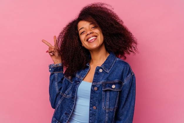 Foto jovem mulher afro-americana isolada na parede rosa alegre e despreocupada, mostrando um símbolo de paz com os dedos.