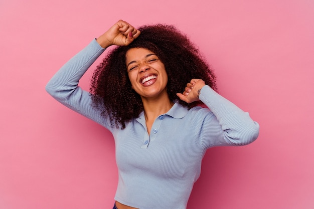 Jovem mulher afro-americana isolada na rosa comemorando um dia especial, pula e levanta os braços com energia.