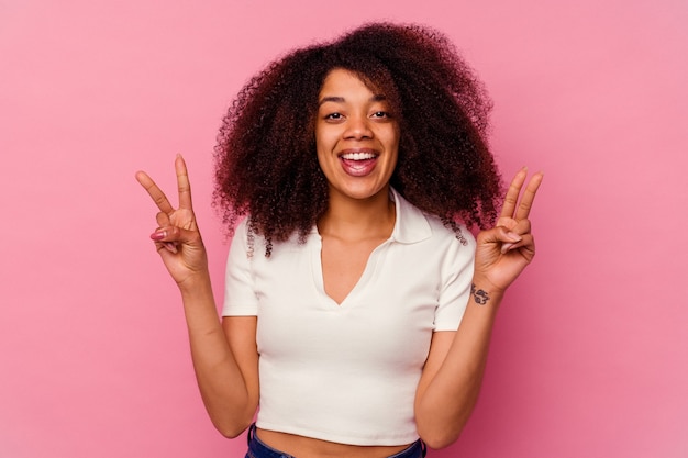 Jovem mulher afro-americana isolada na rosa mostrando sinal de vitória e sorrindo amplamente.