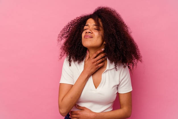 Jovem mulher afro-americana isolada na rosa sofre de dor na garganta devido a um vírus ou infecção.