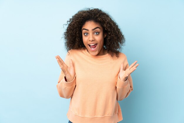 Jovem mulher afro-americana isolada no espaço azul com expressão facial de surpresa