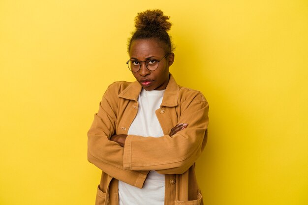 Jovem mulher afro-americana isolada no fundo amarelo, cara carrancuda em desgosto, mantém os braços cruzados.