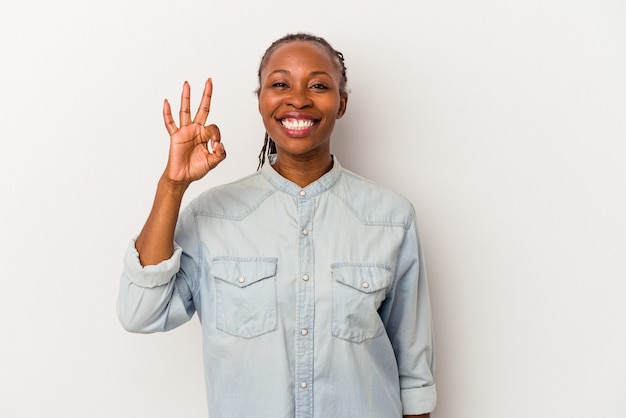 Jovem mulher afro-americana isolada no fundo branco, alegre e confiante, mostrando um gesto de ok.