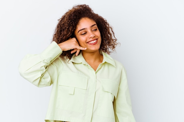 Jovem mulher afro-americana isolada no fundo branco, mostrando um gesto de chamada de telefone móvel com os dedos.