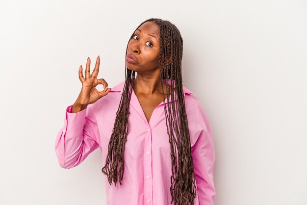 Jovem mulher afro-americana isolada no fundo branco pisca um olho e segura um gesto de ok com a mão.