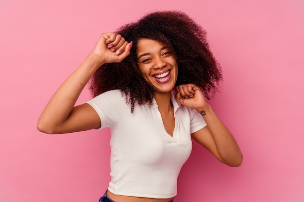 Jovem mulher afro-americana isolada no fundo rosa, dançando e se divertindo.