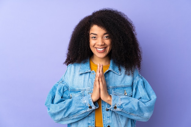 Jovem mulher afro-americana isolada no roxo mantém as palmas unidas. Pessoa pede algo