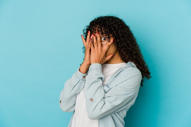 Jovem mulher afro-americana isolada piscar por entre os dedos assustados e nervosos.