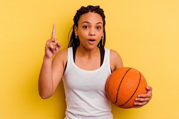 Jovem mulher afro-americana jogando basquete isolado na parede amarela, tendo uma ideia, o conceito de inspiração.