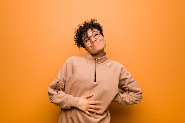 Jovem mulher afro-americana mista contra um marrom toca a barriga, sorri suavemente, conceito de comer e satisfação.