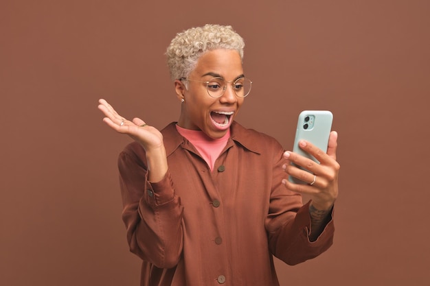 Jovem mulher afro-americana muito feliz com telefone grita e acena as mãos