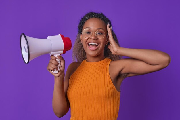 Foto jovem mulher afro-americana olha para a câmera com prazer e segura megafone