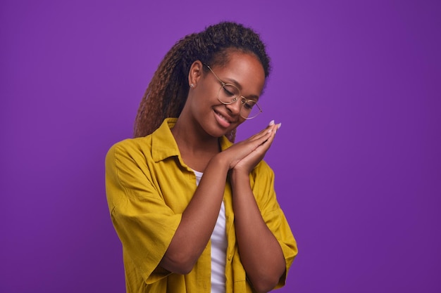 Jovem mulher afro-americana positiva em óculos olha para baixo e sorri