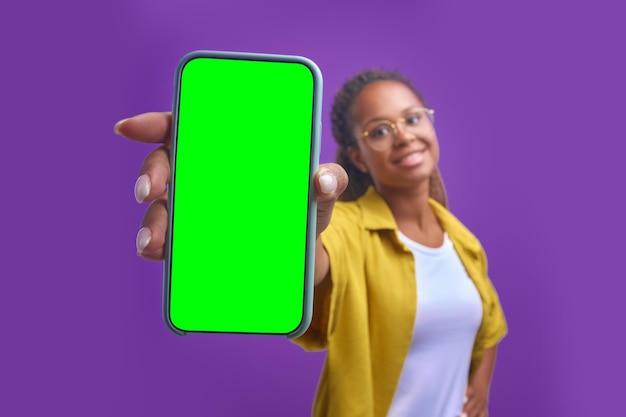 Foto jovem mulher afro-americana positiva estende o telefone de tela verde para a câmera