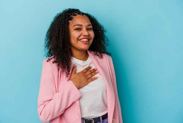 Jovem mulher afro-americana ri alto, mantendo a mão no peito.