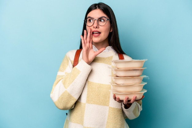 Jovem mulher afro-americana segurando Tupperware isolado em fundo azul gritando e segurando palma perto da boca aberta