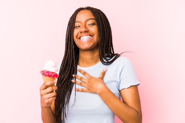 Jovem mulher afro-americana segurando um sorvete isolado ri alto, mantendo a mão no peito.