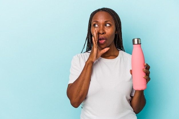 Jovem mulher afro-americana segurando uma cantina isolada em um fundo azul está contando uma notícia secreta de travagem e olhando para o lado