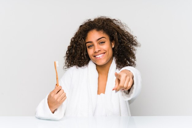 Jovem mulher afro-americana segurando uma escova de dentes, sorrisos alegres, apontando para a frente.