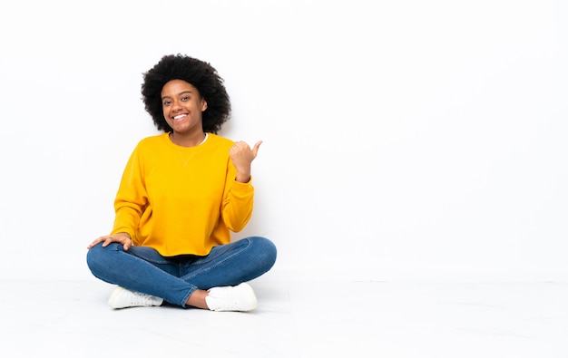 Jovem mulher afro-americana sentada no chão, apontando para o lado para apresentar um produto