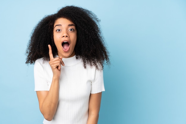 Jovem mulher afro-americana sobre parede, pretendendo realizar a solução enquanto levanta um dedo