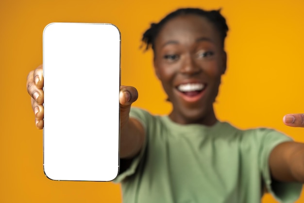 Jovem mulher afro-americana sorridente mostrando smartphone com tela em branco contra fundo amarelo