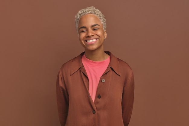 Jovem mulher afro-americana sorridente segurando as mãos atrás das costas fica no estúdio