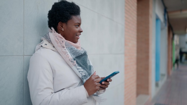 Jovem mulher afro-americana sorrindo confiante usando smartphone na rua