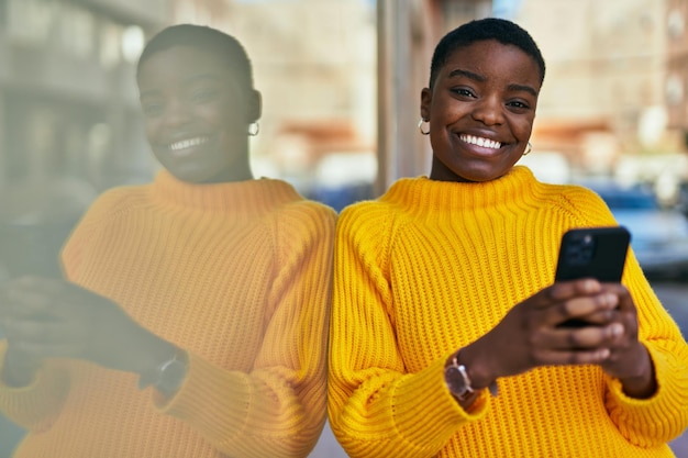 Jovem mulher afro-americana sorrindo feliz usando smartphone na cidade