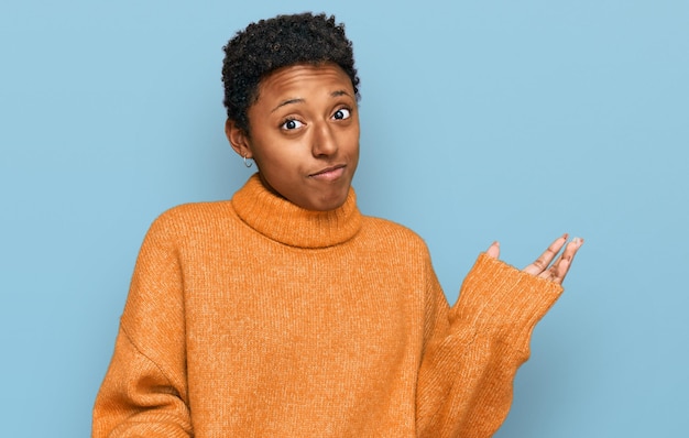 Jovem mulher afro-americana vestindo roupas casuais sem noção e expressão confusa com os braços e as mãos levantadas. conceito de dúvida.