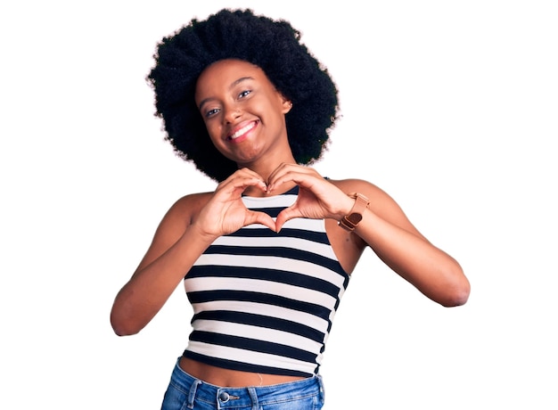 Jovem mulher afro-americana vestindo roupas casuais sorrindo apaixonadamente mostrando o símbolo do coração e a forma com as mãos conceito romântico