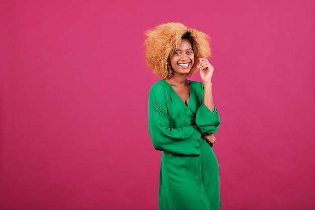 Jovem mulher afro em elegante vestido verde, olhando para a câmera e sorrindo em pé sobre um fundo isolado.