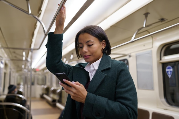 Jovem mulher afro em um trem do metrô usando um celular. Mulher biracial sofre com o vício em smartphone