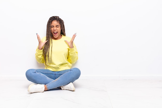 Jovem mulher afro gritando furiosamente, sentindo-se estressada e irritada com as mãos para o alto dizendo por que eu