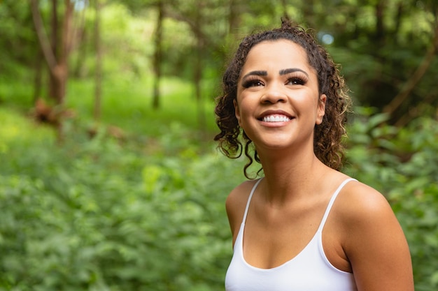 Jovem mulher afro no parque, sorrindo para a câmera.