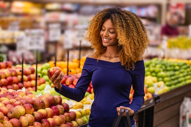 Jovem mulher afro no supermercado, comprando maçãs.