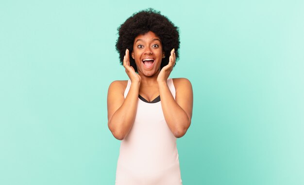 Jovem mulher afro se sentindo chocada e animada, rindo maravilhada e feliz por causa de uma surpresa inesperada