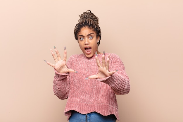 Jovem mulher afro se sentindo feliz, animada e surpresa, olhando para o lado com as duas mãos no rosto